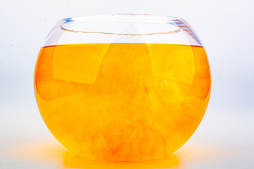 Orange food coloring diffuse in water inside round bowl glass with empty copyspace area for slogan or advertising text message, over isolated white background.