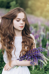 Portrait of young cute brunette girl in lupine violet field in blossom in summer sunset. Greenhouse, nature, natural beauty, freedom, youth concept