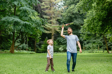 Fototapeta premium Dad and son together launch model airplane outdoors, both man and boy are looking cheerfully at plane. Father and son spending good time together, family relationships concept. Full leight
