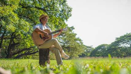 Young asian man playing guitar in park