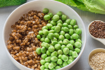 The concept of healthy food. Vegetarian breakfast. Bowl with spelled wheat and green peas, cucumbers, lettuce leaves, seasonings on gray background.