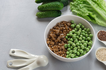 The concept of healthy food. Vegetarian breakfast. Bowl with spelled wheat and green peas, cucumbers, lettuce leaves, seasonings on gray background.