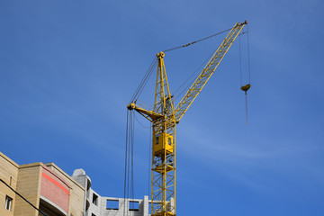 Industrial construction crane hoisting against blue sky. Crane builds a house. Mortgage, new housing, apartment in the city, construction, residential quarters.