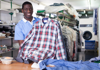 Worker of dry cleaner showing clean clothes