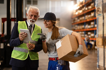 Happy mature businessman and female worker using digital tablet in industrial storage compartment.