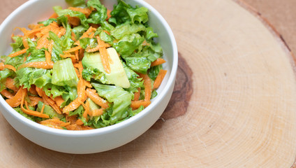 Fresh vegetable salad with greens and avocado, carrots and spinach leaves. Beautiful salad serving on the table, on a wooden stand in rustic style. Сoncept of healthy food, organic food, vegetarian