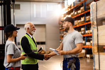 Happy industrial worker shaking hands with senior company manager in a factory.