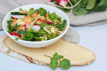 Fresh vegetable salad with greens and radishes, carrots and spinach leaves. Beautiful salad serving on the table, on a wooden stand in rustic style. Сoncept of healthy food, organic food, vegetarian