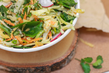 Fresh vegetable salad with greens and radishes, carrots and spinach leaves. Beautiful salad serving on the table, on a wooden stand in rustic style. Сoncept of healthy food, organic food, vegetarian