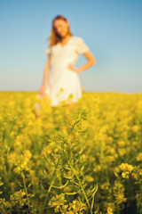 Fototapeta na wymiar Young woman in white dress on a meadow of wild flowers. She put hat in her hand