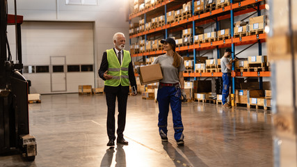 Senior manager talking to female warehouse worker while walking to industrial building.
