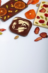 Homemade white and black chocolate. Decorated with slices of dried orange, strawberries, cherries and pistachios. On a white background.