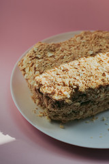 Photo of a delicious fantastic homemade fresh layered honeycomb modern cake on a porcelain white plate on pink background indoor on sunlight rustic style