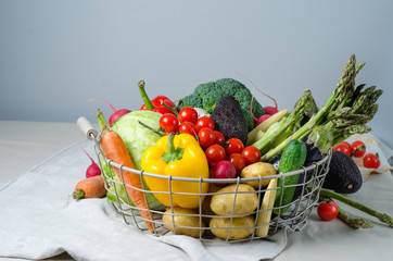 Fresh vegetables in a metal basket on the table. Cherry tomatoes, asparagus, broccoli, potato, peppers, radish, eggplants, zucchini, carrots and onions.