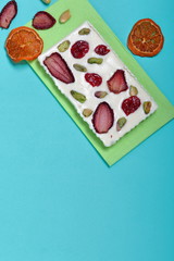 Homemade white chocolate. Decorated with slices of dried orange, strawberries, cherries and pistachios. It lies on a light green napkin on a mint background.