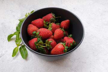 Natural berries, fresh summer dessert. Bowl of fresh sweet red strawberry and mint leaves on gray stone table.
