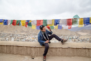 Asia traveler man enjoy with traditional Tibetans Prayer flag in difference five color flags with background of Leh Ladakh city and Himalaya mountain in north of India.