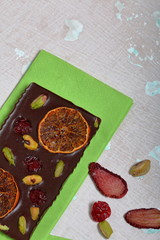 Homemade black chocolate. Decorated with slices of dried orange, strawberries, cherries and pistachios. On an aged surface with peeling paint.