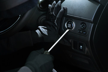 car thief a man in hooded black clothes and wear gloves breaking into switch start button engine...