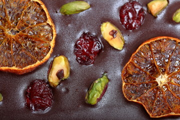 Homemade black chocolate. Decorated with slices of dried orange, cherries and pistachios. Close-up.