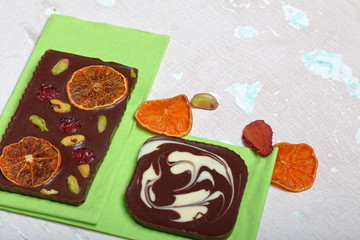 Homemade black chocolate. Decorated with slices of dried orange, strawberries, cherries and pistachios. On an aged surface with peeling paint.