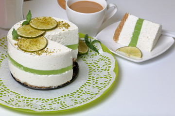 Lime cheesecake without baking. The piece is cut off. Lies on a plate. Near a cup of coffee with milk.