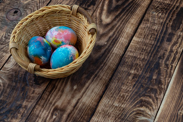 Colorful Easter eggs in a basket on a wooden background, space for text.