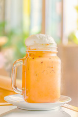 Thai milk tea topped with whipped cream in mason jar mug with handle.