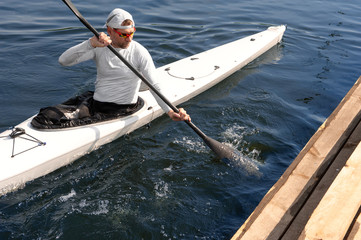 Man paddling a white kayak on the river near the shore. Kayaking concept