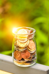 Conceptual image of saving money. Bottle of coins with nature background