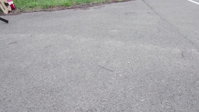 [Static, slow motion] footage of acoustic guitar being destroyed by throwing it on the ground. Classic guitar is smashed on the ground and bounces off. Demolished wooden guitar on the street.