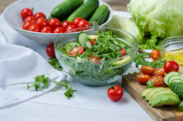 Fresh salad with cucumbers, cherry tomatoes, arugula, avocado, baby corn on white background. Vegetables on wood. Bio Healthy food, herbs and spices. Organic vegetables on wood.
