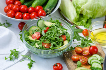 Fresh salad with cucumbers, cherry tomatoes, arugula, avocado, baby corn on white background. Vegetables on wood. Bio Healthy food, herbs and spices. Organic vegetables on wood.