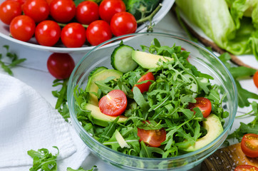 Fresh salad with cucumbers, cherry tomatoes, arugula, avocado, baby corn on white background. Vegetables on wood. Bio Healthy food, herbs and spices. Organic vegetables on wood.