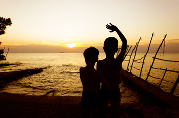 Small boys waving at sunset by the sea