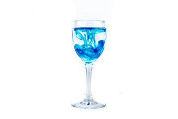 Blue food coloring diffuse in water inside wine glass with empty copyspace area for slogan or advertising text message, over isolated white background.