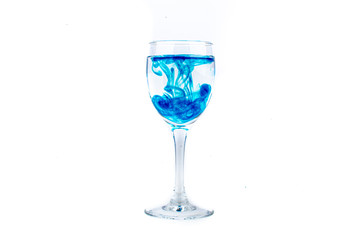Blue food coloring diffuse in water inside wine glass with empty copyspace area for slogan or advertising text message, over isolated white background.