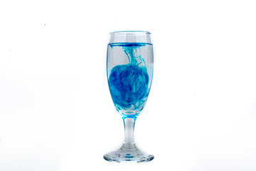 Blue food coloring diffuse in water inside wine glass with empty copyspace area for slogan or advertising text message, over isolated white background.