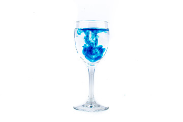 Blue food coloring diffuse in water inside wine glass with empty copyspace area for slogan or advertising text message, over isolated white background.