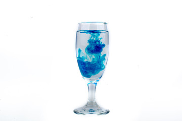 Blue food coloring diffuse in water inside wine glass with empty copyspace area for slogan or advertising text message, over isolated white background.