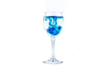 Blue food coloring diffuse in water inside wine glass with empty copyspace area for slogan or advertising text message, over isolated white background.