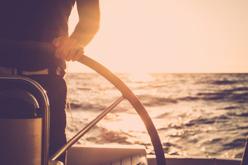 Fototapeta na wymiar Close up of man's hand on sail boat helm - marine ship lifestyle concept of travel for beautiful holiday destination - alternative people life - sunset and sunlight in background on the ocean