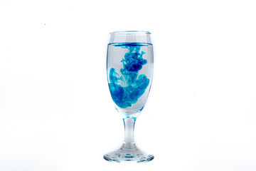 Blue food coloring diffuse in water inside wine glass with empty copyspace area for slogan or advertising text message, over isolated white background.
