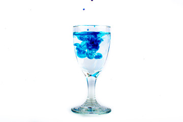 Blue food coloring diffuse in water inside wine glass with empty copyspace area for slogan or advertising text message, over isolated white background.