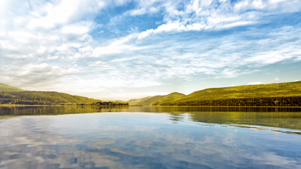Fototapeta premium river water on forest mountains background lake and mountain landscape panorama ground view of beautiful autumn nature with white clouds blue sky and scenery reflection in water travel outdoor concept