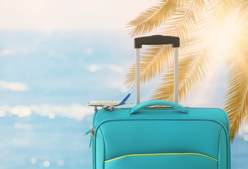 holidays. travel concept. blue suitcase and airplane toy infront of tropical background