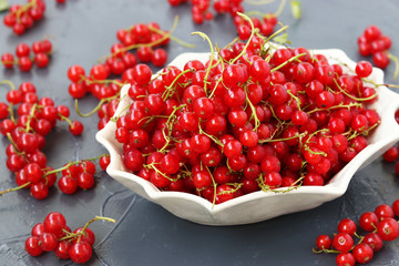Red currant is arbitrarily located in a white plate on a dark background, horizontal photo