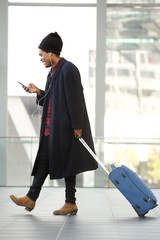 Full length side of african american travel man walking at airport with mobile phone and suitcase