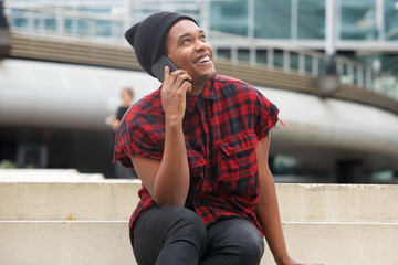 young black man smiling in city and talking with smart phone