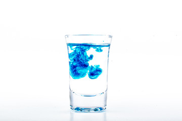 Blue food coloring diffuse in water inside shot glass with empty copyspace area for slogan or advertising text message, over isolated white background.